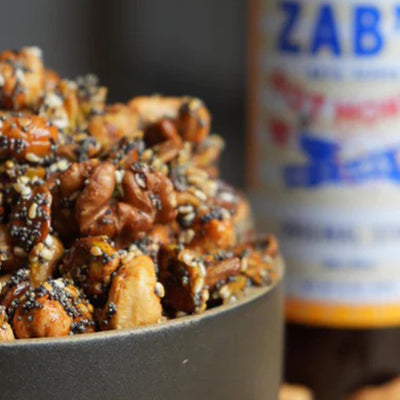 A bowl of nuts with a bottle of honey in the background