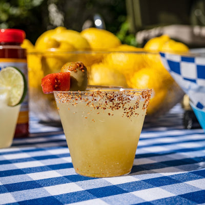 Picture of a green cocktail with tajin on the rim and a fruit skewer