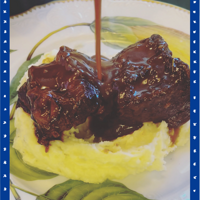plate of short ribs on top of mashed potatoes with sauce dripping onto the dish.