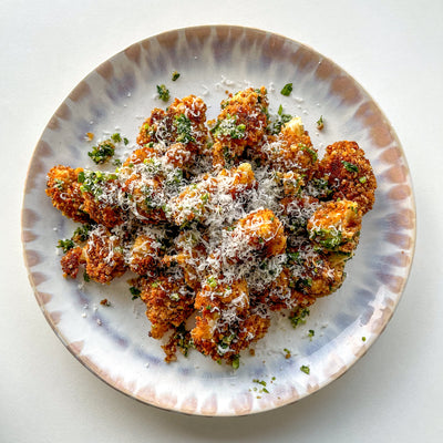 A plate of spicy cauliflower bites with cheese on top.
