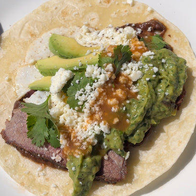 Image of tri tip breakfast taco with fried egg, avocado salsa, cheese and hot sauce
