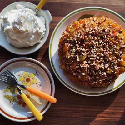 A plate with an apple upside down cake next to a bowl of whipped cream