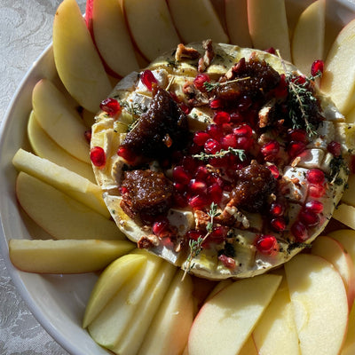 A plate of apple slices with a block of baked brie cheese, topped with pomegranetes