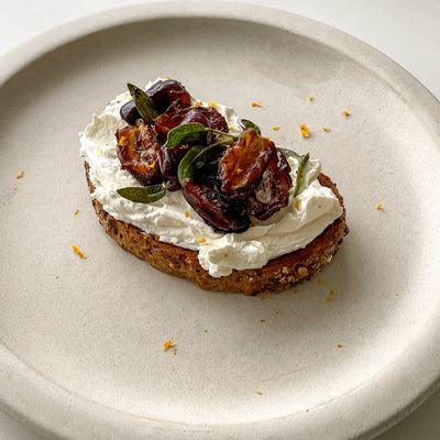 A piece of toast with whipped ricotta cheese, mascarpone cheese, topped with spicy dates and sage leaves